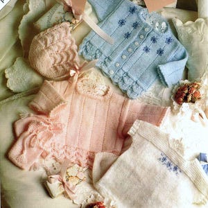 May include: Hand-knitted baby garments in soft pastel colours, including a blue cardigan with floral detailing, a pink sweater, and a white top. The image includes a bonnet and decorative elements, with the text "premature baby".
