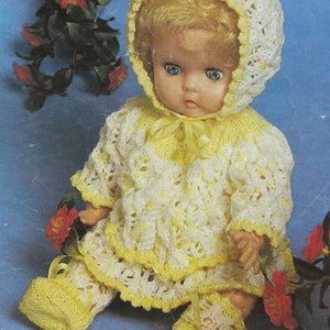May include: A vintage doll wearing a handmade white and yellow knitted outfit, including a bonnet, sweater, skirt, and booties. The doll has blonde hair and blue eyes. The outfit is trimmed with yellow ribbon. The doll is sitting on a blue background.