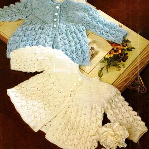 Könnte beinhalten: Zwei gestrickte Babyjacken, eine in hellblau und eine in weiß, mit Knopfleiste und zartem Spitzenmuster.