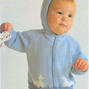 May include: A light blue knitted baby jacket with a hood and a zip fastening. The jacket has a duck design on the lower front. The baby is wearing the jacket. The jacket is made of soft, knitted material.