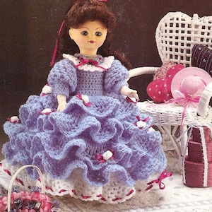 May include: A crocheted doll dress in a light purple color with white and pink accents. The dress has a ruffled skirt and is designed for a 11 1/2 inch porcelain-look doll.