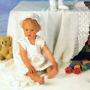 May include: A white crocheted baby dress with a matching hat and booties. The baby is sitting on a white crocheted blanket with colorful wooden blocks.
