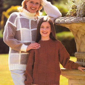 May include: A woman and a girl wearing knitted sweaters. The woman's sweater is white, brown, and gray with a checkered pattern. The girl's sweater is brown with a checkered pattern. Both are wearing white pants.