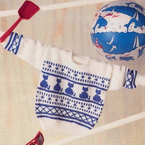 May include: White knitted baby sweater with a blue and white cat pattern. The sweater has a round neckline and long sleeves.