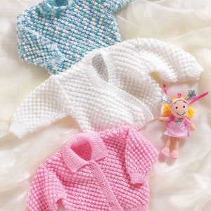 Könnte beinhalten: Drei gestrickte Baby-Pullover in verschiedenen Farben: blau und weiß, weiß und rosa. Die Pullover haben ein strukturiertes, Noppen-Design.