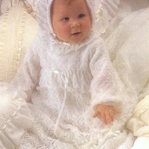 May include: White knitted baby dress and bonnet set with a delicate lace pattern. The dress has a long, flowing skirt and a fitted bodice. The bonnet has a wide brim and a bow at the top. The set is perfect for a special occasion.