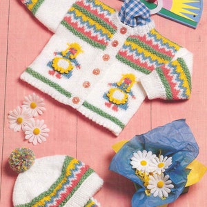 Puede incluir: Un cárdigan de punto blanco con un patrón de zigzag colorido y dos muñecas bordadas. El cárdigan tiene botones en la parte delantera. Un gorro de punto blanco a juego con un patrón de zigzag colorido y un pompón en la parte superior.