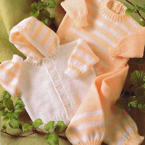 May include: A selection of knitted baby clothes in pastel shades. The set includes a hooded cardigan, a sweater, and trousers. The garments feature a striped pattern in white and peach, with ribbed cuffs and hems. The clothes are displayed on a green surface.
