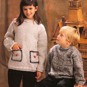 May include: Two children in knitted sweaters. The girl's sweater is light grey with two square pockets, each with a red heart design and black trim. The boy's sweater is a darker grey with a single pocket. Both have long sleeves.
