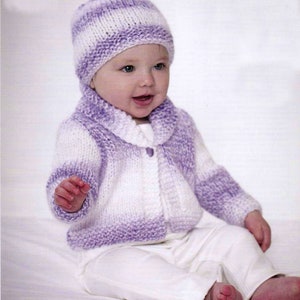 May include: A baby wearing a white and purple striped knitted cardigan with a matching hat. The cardigan has a button closure and a collar.