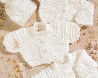 May include: Three white knitted baby cardigans with button closures. The cardigans are arranged on a light pink background with white flowers and ribbons.