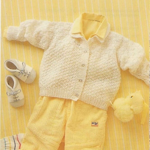 May include: A white knitted cardigan with a button fastening, yellow corduroy trousers, and a yellow stuffed toy. The cardigan has a collar and long sleeves.