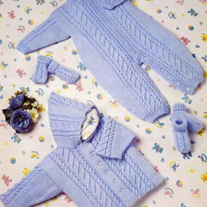May include: A light blue knitted baby outfit set, including a hooded jacket, a one-piece suit, and matching booties. The set features a cable knit design and is displayed on a patterned surface. The jacket has button closures.