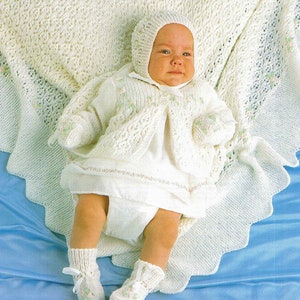 May include: A white knitted baby outfit with a matching hat, booties, and a blanket. The outfit features a delicate floral design and a lace trim.