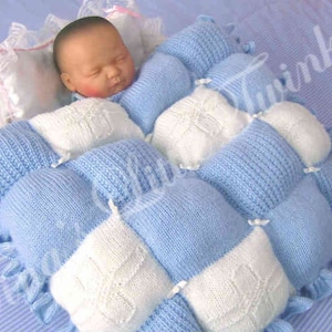 May include: A blue and white knitted baby blanket with a ruffled edge. The blanket is made of squares and is ideal for a newborn.