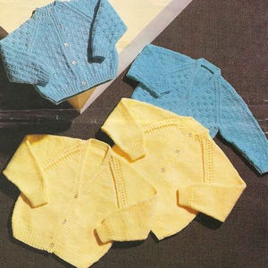 May include: A selection of knitted baby cardigans in blue and yellow. The cardigans feature button fastenings and textured knit patterns. The garments are arranged on a dark brown surface, highlighting the different colours and styles of the knitwear.