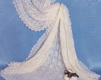 May include: A cream-coloured, intricately crocheted shawl with a scalloped edge. The shawl is draped over a surface, with a pair of small, white baby shoes with navy bows resting on the shawl. The background is a solid light blue.