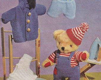 May include: A knitted teddy bear wearing blue overalls, a red and white striped shirt, and a red and white striped hat. The bear is standing on a wooden stool next to a blue basket and a wooden ironing board with an iron on it. There are also knitted clothes hanging on a wooden clothes rack.
