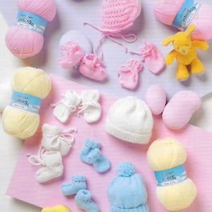 Könnte beinhalten: Eine Sammlung von Strickzubehör für Babys, darunter Garn, eine Mütze, Booties und Fäustlinge. Das Garn ist in den Farben Rosa, Gelb und Blau. Die Strickprojekte sind in Weiß, Rosa und Blau.