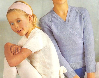 May include: Two girls wearing white and light blue knit sweaters. The girl on the left is wearing a pink headband and white tights. The girl on the right is wearing a blue headband and blue pants.