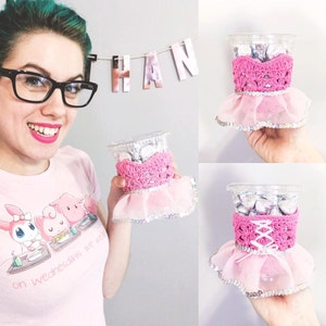 May include: Three clear plastic cups with pink crocheted ballerina tutus and silver glitter trim. The cups are filled with chocolate candies.