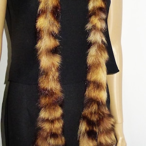 May include: A brown and tan fur stole with a striped pattern. The stole is draped over a black dress, creating a contrast in textures and colours. The fur appears soft and luxurious.