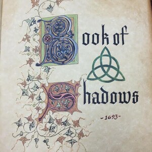 May include: An antique book cover with an ornate, illuminated title page. The title is "Book of Shadows" with a green triquetra symbol and the date "1693". The letters "B" and "S" are decorated with intricate floral designs.