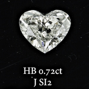 May include: A heart-shaped diamond, clear and sparkling, with multiple facets. The image shows the diamond against a black backdrop. Text at the bottom reads "HB 0.72ct J SI2".