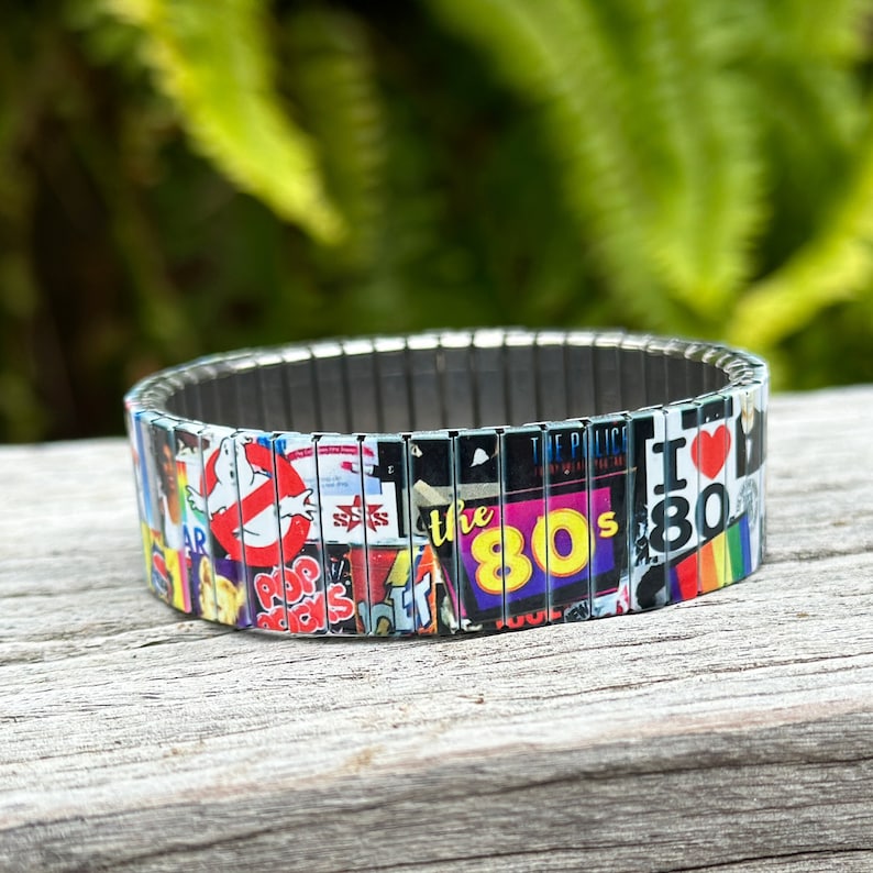May include: A silver expandable bracelet with a colorful collage of 1980s pop culture icons, including Ghostbusters, the words "the 80s", and "I Love the 80s".