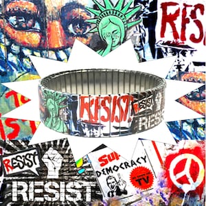 Può includere: Un braccialetto espandibile argentato con un design colorato che presenta la parola "Resist" e immagini della Statua della Liberté e un simbolo di pace. Il braccialetto è realizzato con maglie di metallo e ha un design elastico.