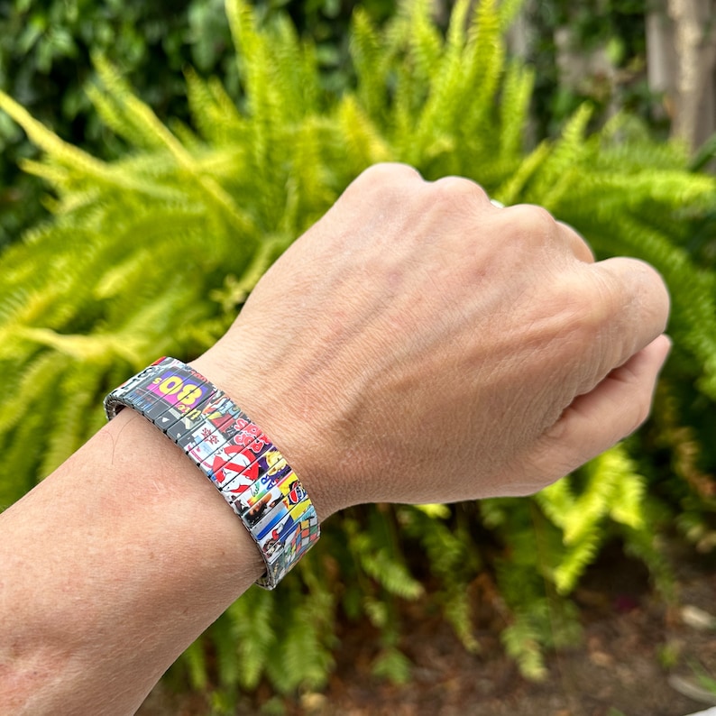 May include: A colorful bracelet made of multiple small squares with different patterns and colors. The bracelet is made of metal and has a flexible design.