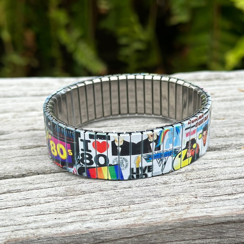 May include: A silver expandable bracelet with a colorful collage of 1980s pop culture icons, including the words "I Love 80s", "Live Aid", and "Wham!"