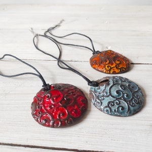 Op de afbeelding: Drie keramische hangers met zwarte koorden. De hangers zijn rond en hebben een draaiend patroon. De hangers zijn rood, oranje en blauw.