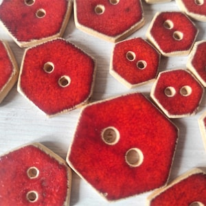 May include: A collection of red ceramic buttons with two holes each. The buttons are octagonal in shape and have a textured surface.