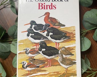 May include: The Oxford Book of Birds, a hardcover book with a white cover and colorful illustrations of various birds on a sandy beach.
