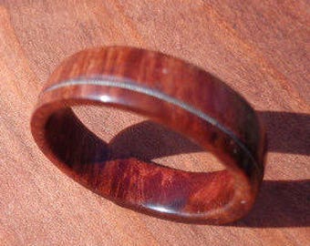 May include: A wooden ring with a thin silver inlay. The ring is dark brown with a reddish hue.