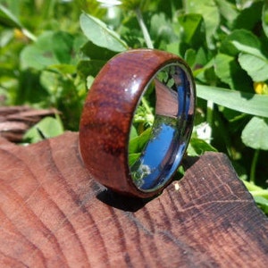 May include: A brown wooden ring with a silver band. The ring is sitting on a wooden surface.