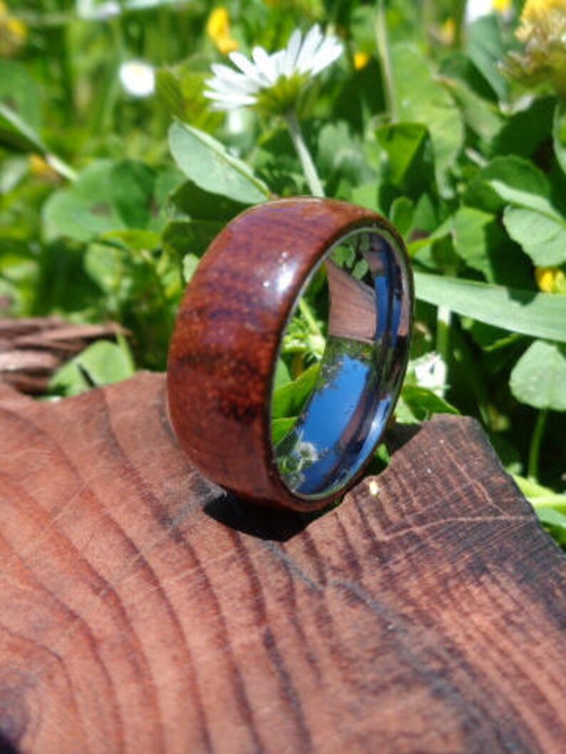 May include: A brown wooden ring with a silver band. The ring is sitting on a wooden surface.