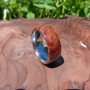 May include: A wooden ring with a silver band. The wood is a dark reddish brown with a natural grain pattern. The ring is sitting on a wooden surface.