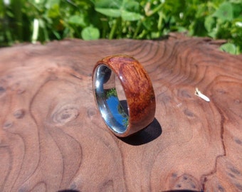 May include: A wooden ring with a silver band. The wood is a dark reddish brown with a natural grain pattern. The ring is sitting on a wooden surface.
