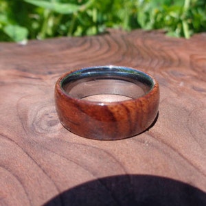 May include: A wooden ring with a silver band. The wood is a dark reddish brown with a natural grain pattern.