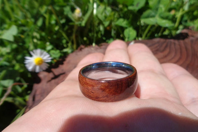 May include: A wooden ring with a dark brown wood grain and a silver metal band. The ring is on a person's finger.
