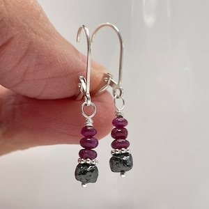 May include: A pair of silver dangle earrings with a black diamond and pink ruby beads.