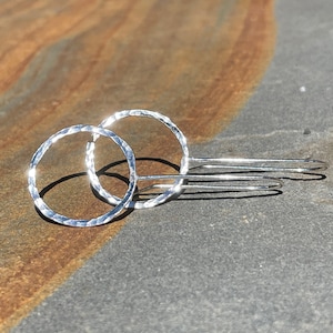 Puede incluir: Un par de pendientes de aro de plata con textura martillada. Los pendientes son simples y elegantes.