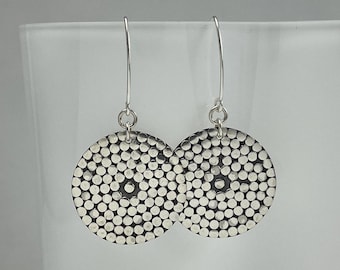 May include: A pair of silver dangle earrings with a circular design. The earrings are made of small, round beads that are arranged in a circular pattern. The earrings are hanging from silver hooks.