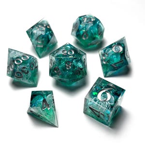 May include: A set of seven polyhedral dice for tabletop games. The dice are a translucent teal color with silver numbering and internal designs. The set includes a D4, D6, D8, D10, D12, D20, and a percentile die.