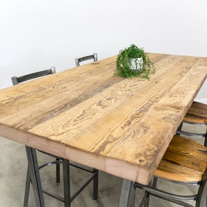 May include: A rustic wooden dining table with a natural wood finish and a live edge. The table is surrounded by four black metal chairs with wooden seats.