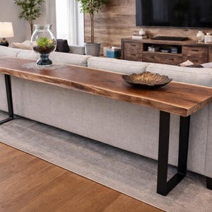 May include: A live edge walnut sofa table with black metal legs. The table is approximately 72 inches long and 14 inches wide. A decorative bowl sits on the table. The table is placed behind a light gray sofa.
