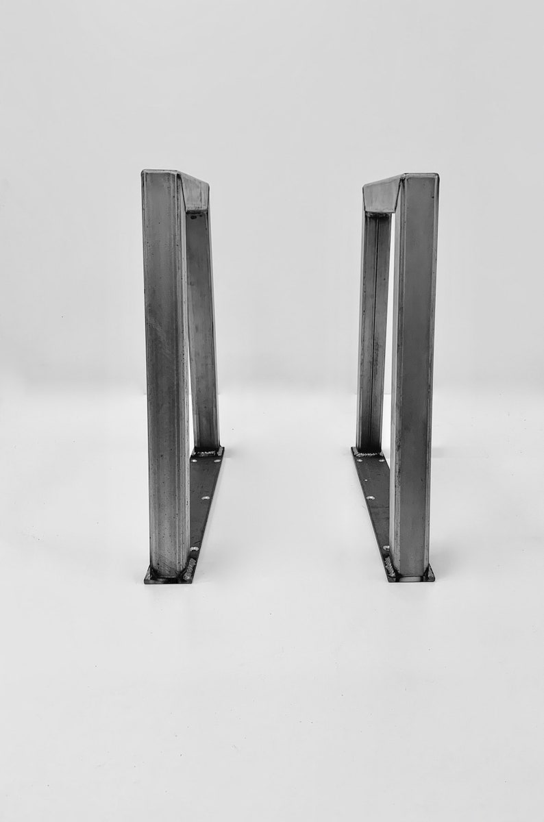 May include: Two metal table legs with a triangular shape and a rectangular base. The legs are made of steel and have a silver finish.