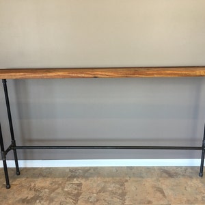 May include: A rustic console table with a reclaimed wood top and black pipe legs. The table has a long, rectangular top and a lower support bar. The wood top has a natural, warm colour, and the metal legs are industrial-style.